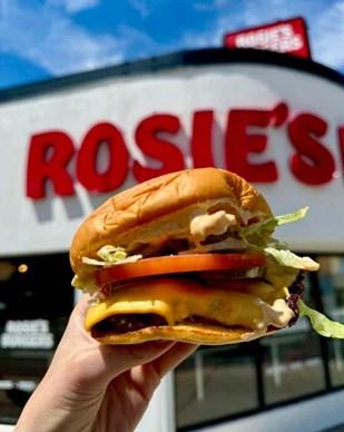 A hand holding a burger in front of a sign
AI-generated content may be incorrect.